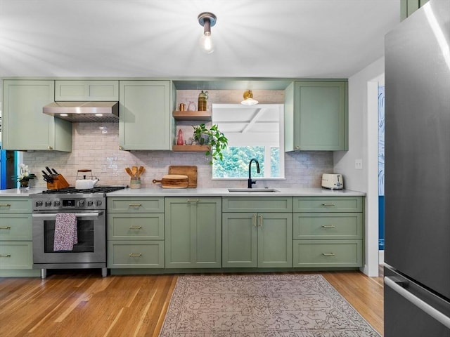 kitchen featuring green cabinets, appliances with stainless steel finishes, range hood, and a sink