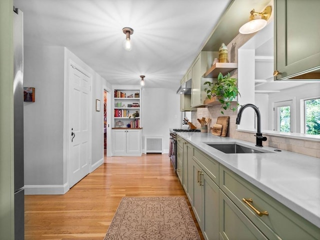 kitchen with a sink, green cabinets, light countertops, under cabinet range hood, and stainless steel stove