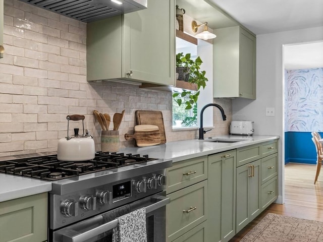 kitchen featuring green cabinets, gas range, a sink, and exhaust hood