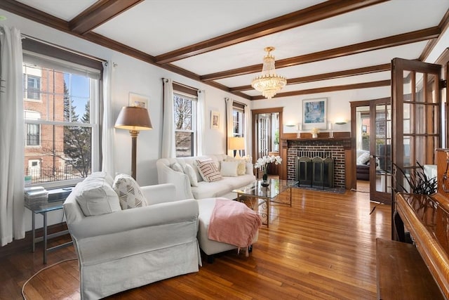 living room featuring beamed ceiling, an inviting chandelier, hardwood / wood-style floors, and a brick fireplace