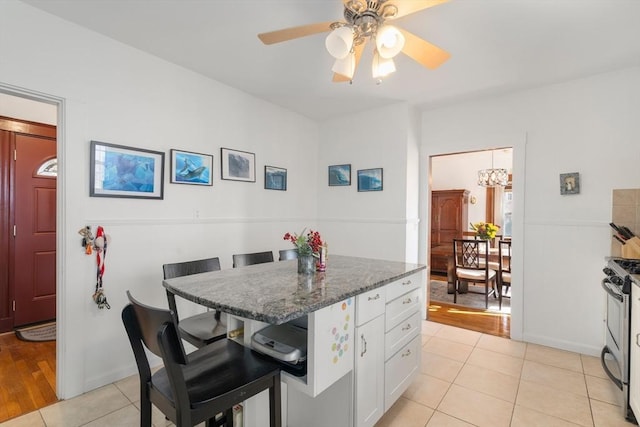 kitchen featuring white cabinetry, a kitchen breakfast bar, light tile patterned flooring, gas range, and dark stone counters