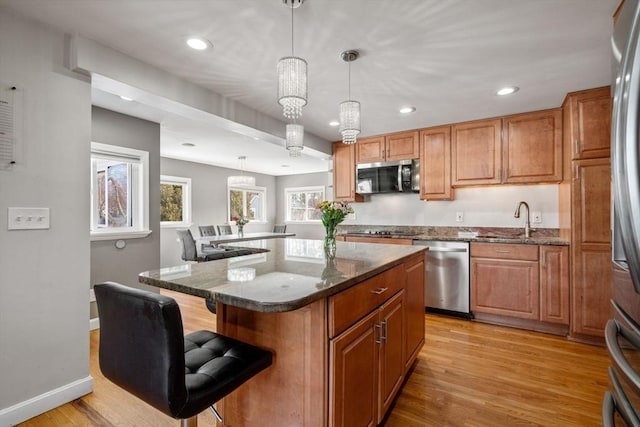 kitchen featuring appliances with stainless steel finishes, dark stone counters, light wood-type flooring, and a sink