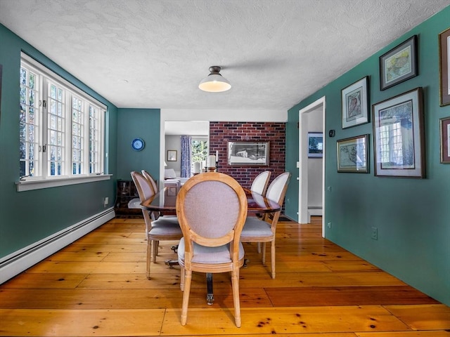 dining space featuring light wood-style floors, a baseboard radiator, a brick fireplace, and a textured ceiling