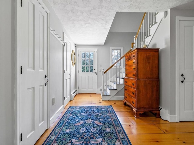 entrance foyer with stairs, baseboards, a baseboard heating unit, and light wood finished floors