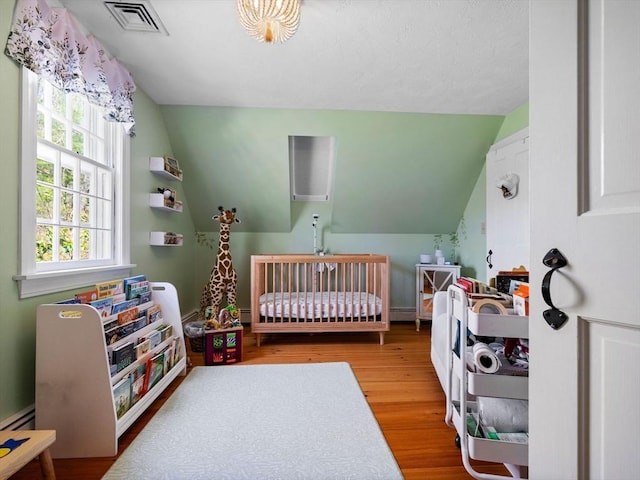 bedroom featuring vaulted ceiling, a crib, wood finished floors, and visible vents