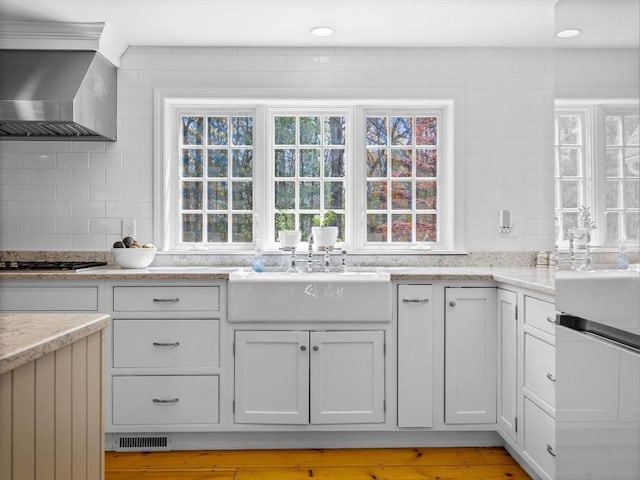 kitchen with wall chimney range hood, visible vents, tasteful backsplash, a sink, and stainless steel gas stovetop
