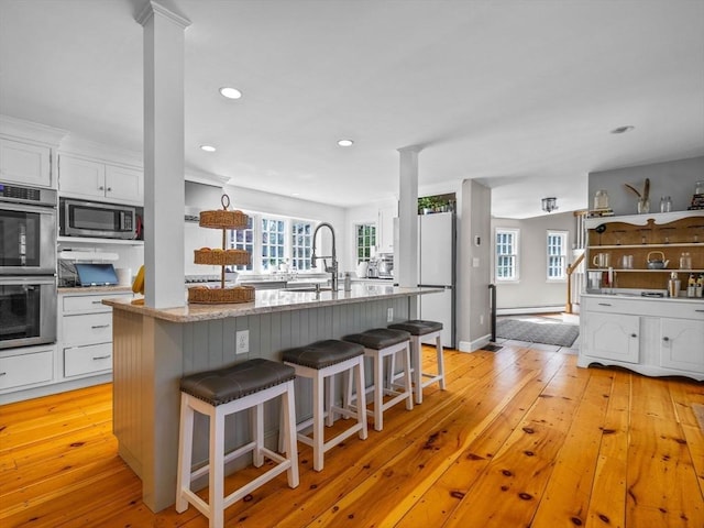 kitchen featuring a kitchen island with sink, a sink, white cabinets, a breakfast bar, and stainless steel appliances