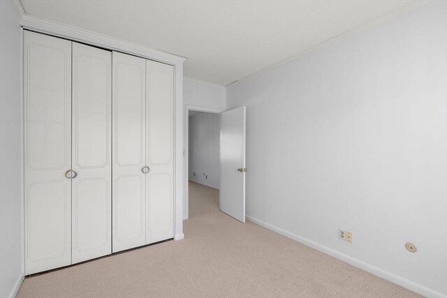 unfurnished bedroom with light carpet, ornamental molding, a closet, and baseboards