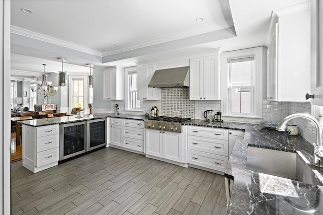 kitchen with a sink, beverage cooler, wall chimney exhaust hood, stainless steel gas cooktop, and ornamental molding
