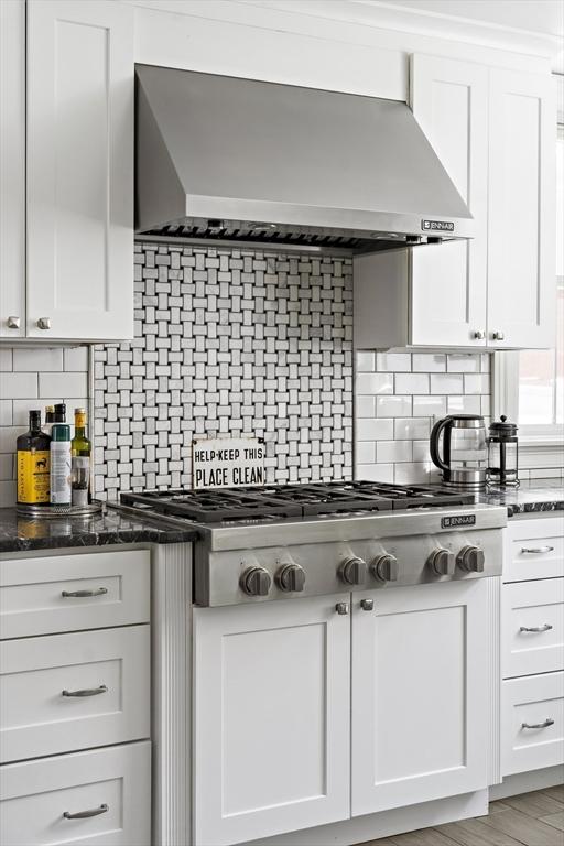 kitchen with wall chimney range hood, decorative backsplash, dark stone counters, and white cabinets