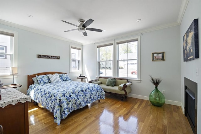 bedroom with wood finished floors, crown molding, a fireplace, ceiling fan, and baseboards