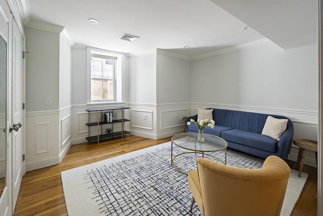 living area featuring wood finished floors, ornamental molding, wainscoting, and a decorative wall