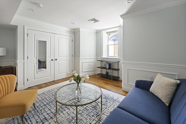 living room with wood finished floors, ornamental molding, wainscoting, and a decorative wall