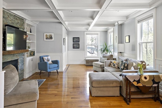 living area featuring a stone fireplace, light wood-style flooring, beam ceiling, coffered ceiling, and ornamental molding