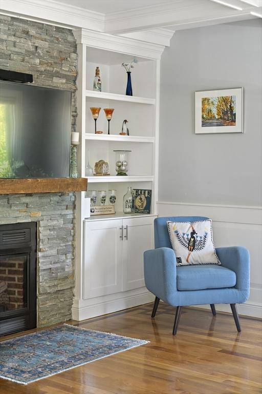 sitting room featuring wood finished floors, wainscoting, built in features, a stone fireplace, and crown molding