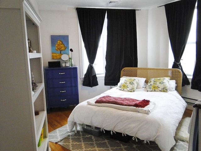 bedroom with dark hardwood / wood-style flooring, a baseboard radiator, and multiple windows