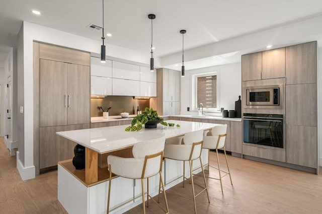 31 Evergreen St Unit 2, Boston, MA 02130 - kitchen featuring black oven, modern cabinets, stainless steel microwave, light wood-style flooring, and a kitchen bar