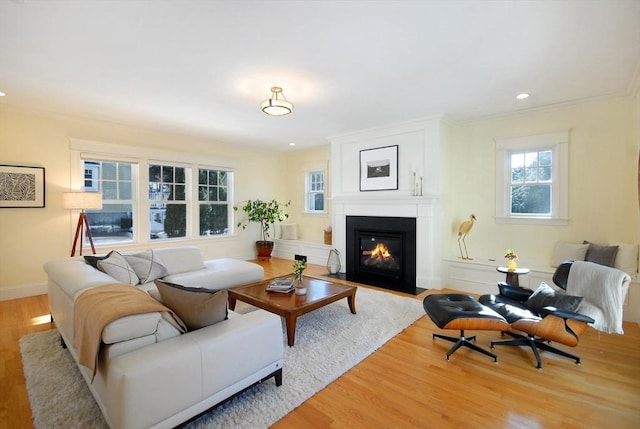 living area with light wood-type flooring, a fireplace with flush hearth, ornamental molding, and recessed lighting