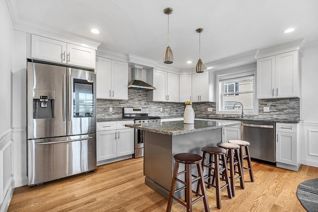 3 Lowell St Unit 1, Waltham, MA 02453 - kitchen featuring appliances with stainless steel finishes, wall chimney exhaust hood, light wood finished floors, decorative backsplash, and a kitchen breakfast bar