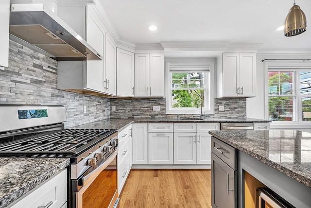 3 Lowell St Unit 1, Waltham, MA 02453 - kitchen featuring stainless steel gas stove, wall chimney exhaust hood, light wood-style floors, white cabinetry, and tasteful backsplash