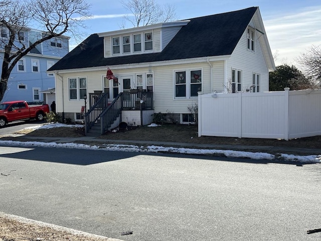 view of front facade featuring a shingled roof and fence