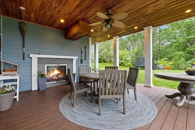 14 Reiling Pond Rd, Lincoln, MA 01773 - wooden terrace featuring a warm lit fireplace, outdoor dining area, a ceiling fan, a yard, and a trampoline