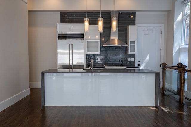 kitchen featuring white cabinetry, wall chimney exhaust hood, appliances with stainless steel finishes, decorative light fixtures, and dark hardwood / wood-style flooring