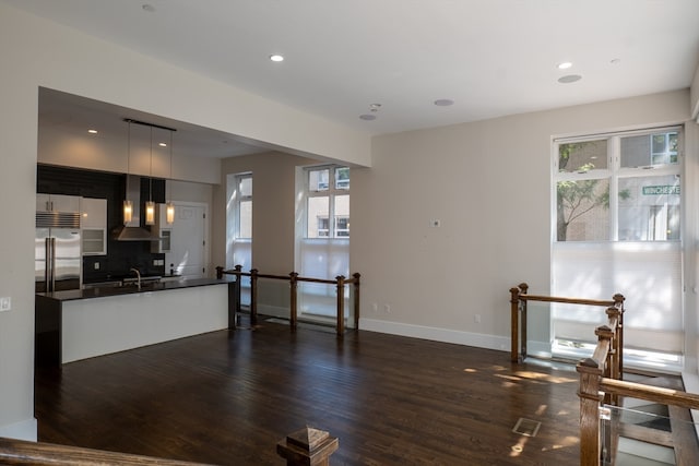 kitchen featuring hanging light fixtures, dark wood-type flooring, sink, wall chimney range hood, and stainless steel built in fridge