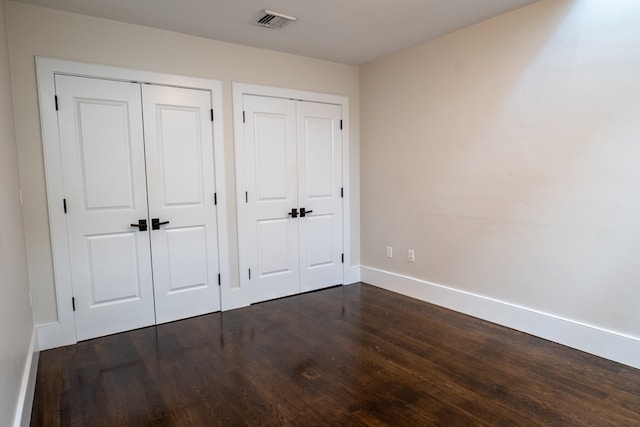 unfurnished bedroom with multiple closets and dark wood-type flooring