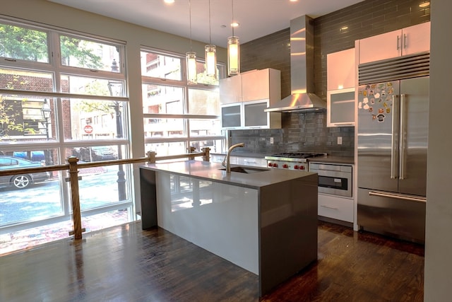 kitchen featuring stainless steel appliances, decorative light fixtures, dark hardwood / wood-style floors, wall chimney range hood, and sink