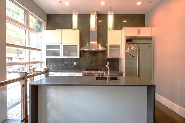 kitchen with hanging light fixtures, a kitchen island with sink, wall chimney exhaust hood, stainless steel appliances, and dark hardwood / wood-style flooring