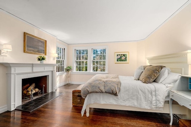 bedroom with baseboards, wood finished floors, and a tile fireplace