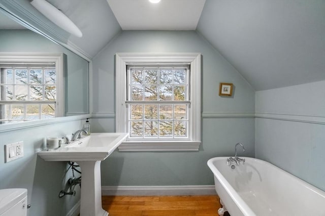 bathroom with lofted ceiling, toilet, wood finished floors, baseboards, and a soaking tub