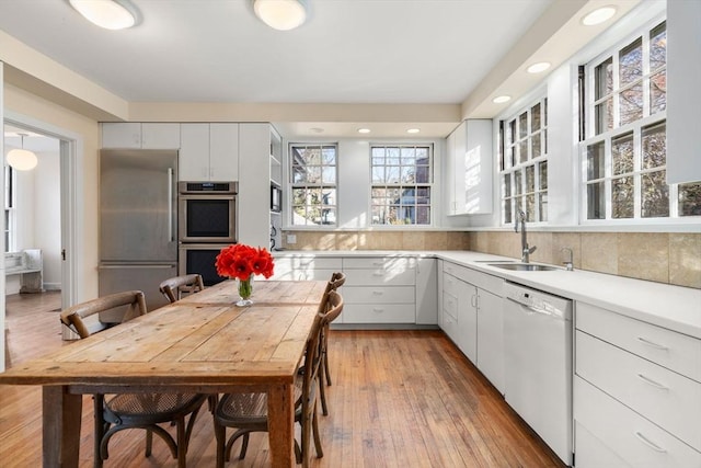 kitchen featuring white cabinets, appliances with stainless steel finishes, light countertops, light wood-style floors, and a sink