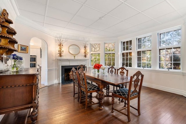 dining room with arched walkways, dark wood-style flooring, a fireplace with flush hearth, and crown molding