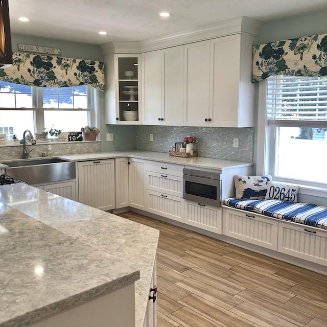 14 Highland St, Clinton, MA 01510 - kitchen featuring stainless steel microwave, light wood-style flooring, white cabinets, decorative backsplash, and glass insert cabinets