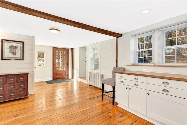 interior space featuring radiator, light wood-style floors, white cabinets, and beamed ceiling