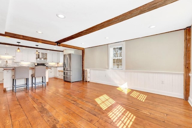 unfurnished living room with recessed lighting, a wainscoted wall, a sink, light wood-type flooring, and beamed ceiling