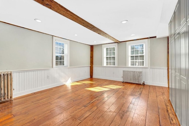 spare room featuring radiator, light wood-style flooring, beamed ceiling, and wainscoting