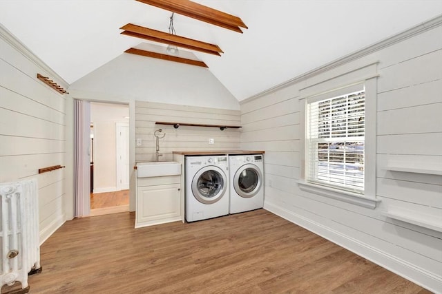 washroom with laundry area, radiator, light wood-type flooring, washing machine and dryer, and a sink