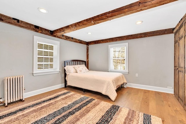 bedroom featuring light wood finished floors, radiator heating unit, baseboards, and beamed ceiling