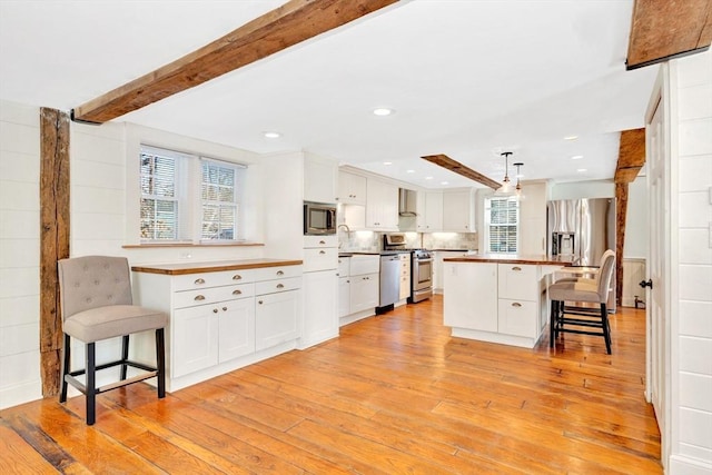 kitchen featuring beam ceiling, a breakfast bar area, light wood-style flooring, appliances with stainless steel finishes, and white cabinetry