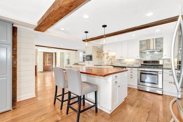 kitchen featuring wall chimney range hood, light wood-style flooring, wood counters, and stainless steel appliances