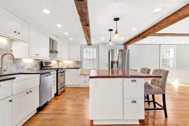 kitchen featuring appliances with stainless steel finishes, beam ceiling, butcher block counters, and a kitchen bar