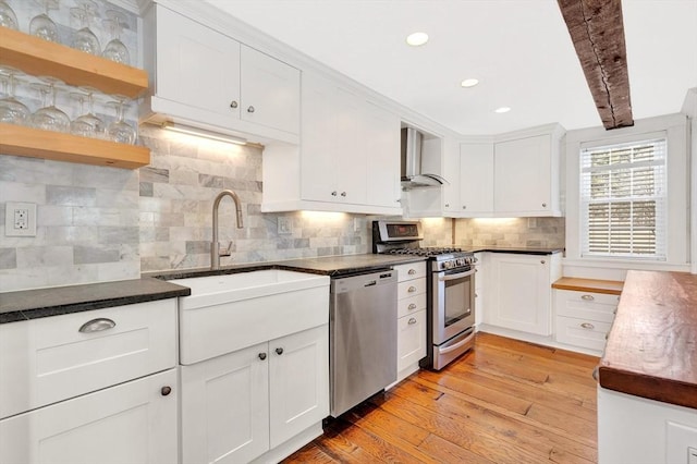 kitchen featuring wall chimney exhaust hood, stainless steel appliances, light wood-type flooring, white cabinetry, and a sink