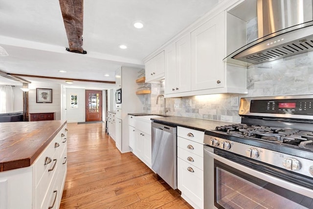 kitchen featuring butcher block counters, appliances with stainless steel finishes, light wood-style floors, a sink, and wall chimney exhaust hood