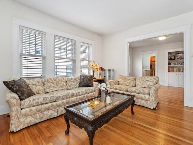 living room with built in shelves, radiator heating unit, and hardwood / wood-style floors