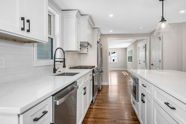 kitchen with wall chimney range hood, a sink, stainless steel appliances, white cabinetry, and dark wood-style floors