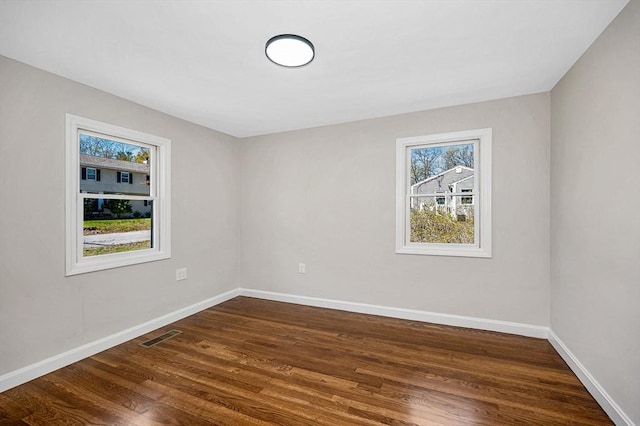unfurnished room featuring baseboards, plenty of natural light, visible vents, and dark wood-type flooring