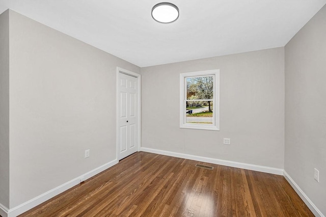 empty room featuring baseboards, wood finished floors, and visible vents